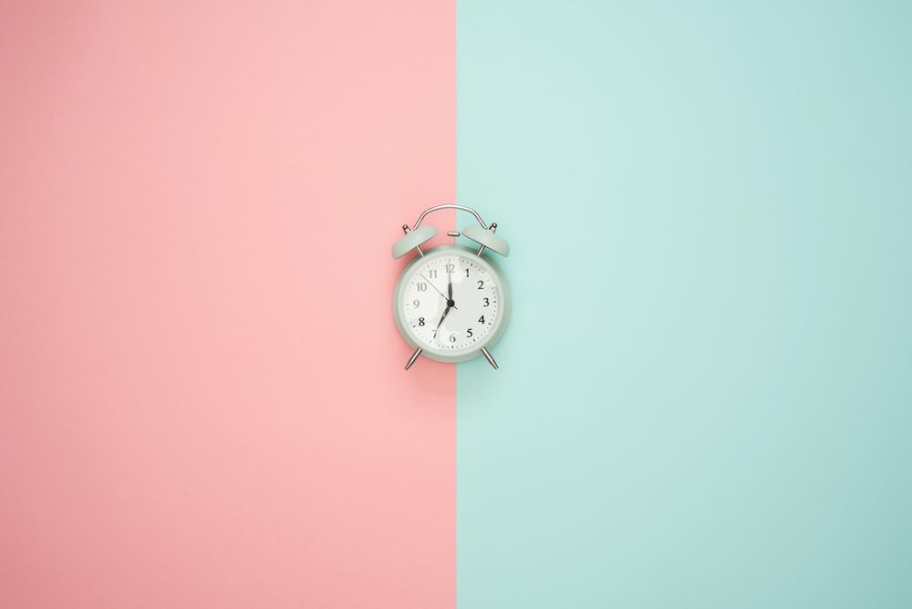 パステル調のピンクとブルーを背景に時計が鎮座する画像。