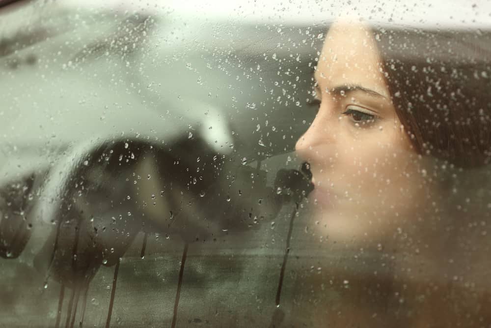 雨の日に車のなかで虚ろ気な表情を浮かべる女性の画像。
